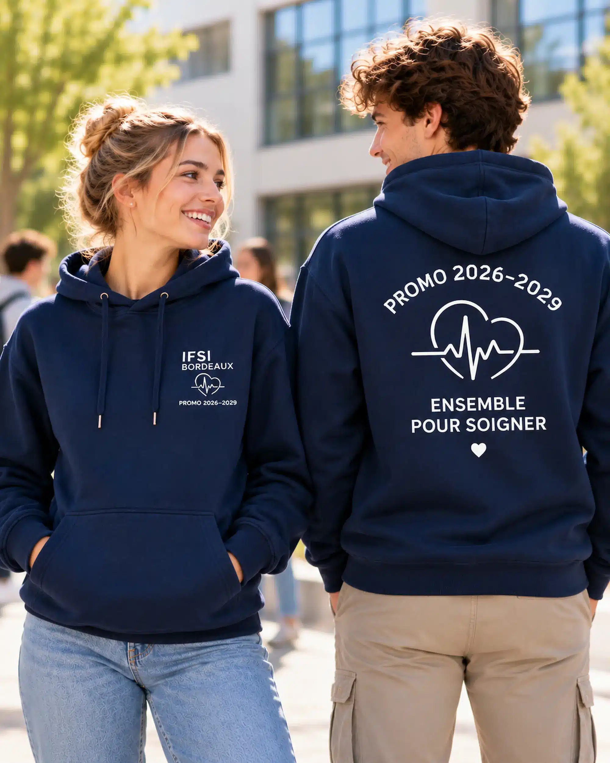 Deux étudiants présentant un sweat à capuche bleu marine personnalisé pour une promotion IFSI, avec impression blanche sur la poitrine et au dos.